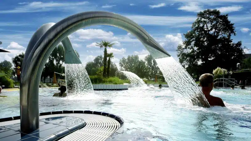 an outdoor pool with water fountains and palm 